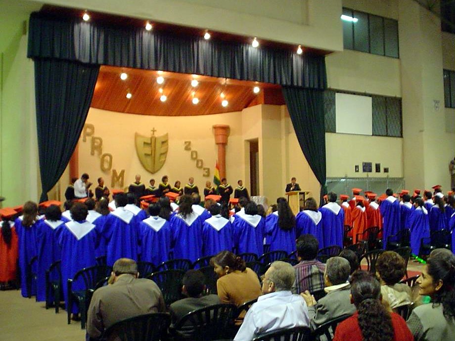 RHEMA Bolivia graduation ceremony in Cochabamba, 2003: graduates in blue and red robes facing the stage