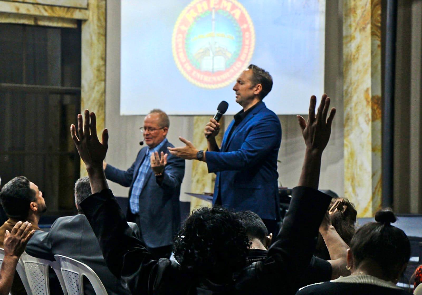 People raising their hands in worship as David and a guest minister lead from the stage